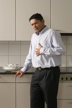 Man in his late thirties standing in his kitchen having a dose of heartburn after a meal.
