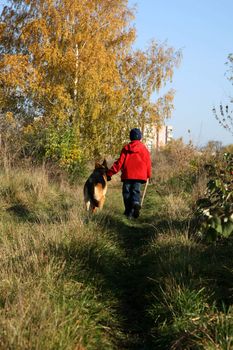 Little boy on the walk with the big, obedient dog (German Shepherd ) on suburb of the city.