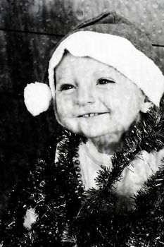 Happy baby playing with Christmas decorations seen through rainy glass