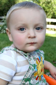 Cute blond baby boy sitting outside in the garden