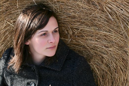 Beautiful brunette female sitting against a hay bale