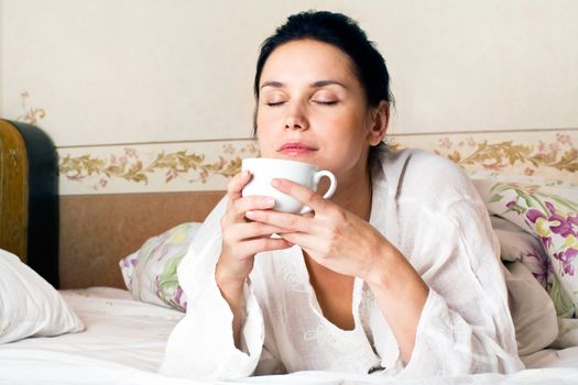 A young woman dreaming and holding white a cup of coffee on bed at bedroom