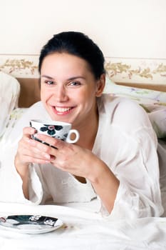 A young happy woman with a cup of coffee in the bed 