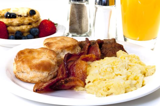 Big country breakfast with scrambled eggs, bacon, buttermilk biscuits, waffles, fruit, and orange juice.