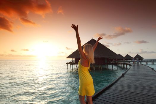 woman in a dress on a bridge home sea and the maldivian sunset on the background