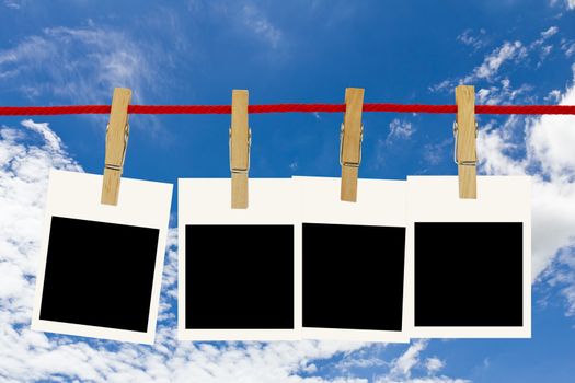 Blank photo frames hang by wooden peg on blue sky