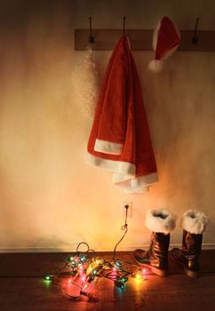 Santa costume hanging on coat hook with christmas lights on floor