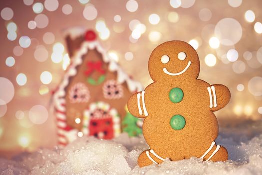 Gingerbread man cookie standing in snow beside house 