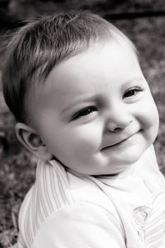 Adorable baby boy sitting outside in the sunny garden 