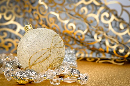 Golden christmas ball with decorations on golden surface and blured backdrop.