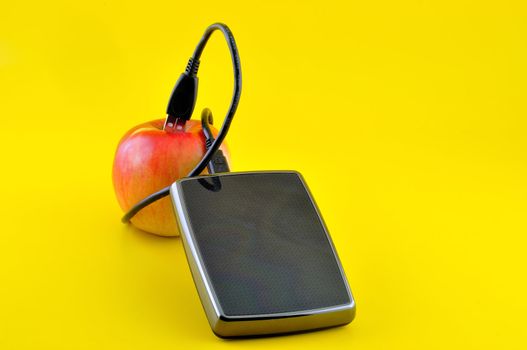 hard disk and a cable that leads from a apple, photographed against a yellow background