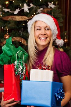 Portrait of beautiful young woman in Santa hat smiling while holding gift boxes.