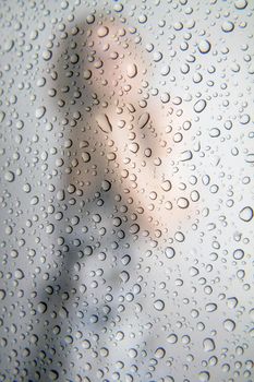 Female silhouette through the raindrops on the glass