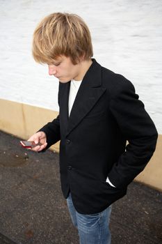 Teenage boy text messaging with mobile phone in street