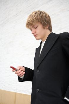 Teenage boy text messaging with mobile phone by white wall