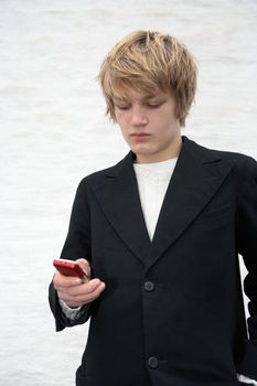 Teenage boy text messaging with mobile phone, white wall in background