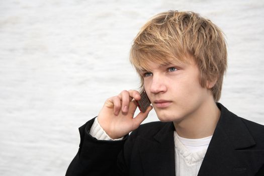 Teenage boy using mobile phone outdoor, wall in background