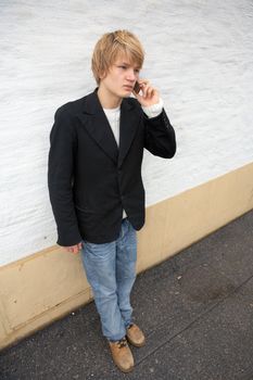Teenage boy using mobile phone, leaning against wall