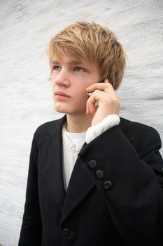Teenage boy using mobile phone by white wall outdoors