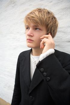 Teenage boy with mobile phone by white wall outdoors