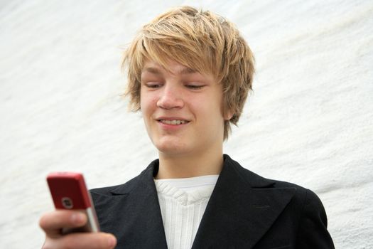 Teenage boy looking at mobile phone by building wall, smiling