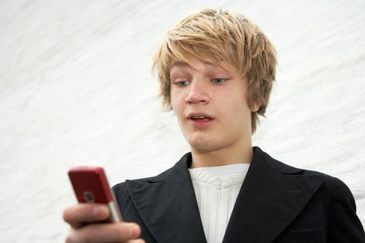 Teenage boy looking at mobile phone by building wall, surprised expression