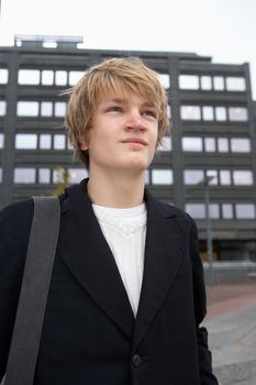 Portrait of happy teenage boy by urban building, carrying shoulder bag