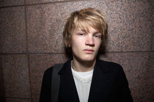 Teenage boy leaning against outside wall, looking at camera