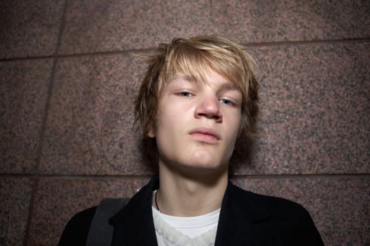 Teenage boy leaning against outside wall, looking at camera, low angle shot