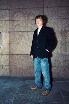 Teenage boy standing by building wall, looking at camera