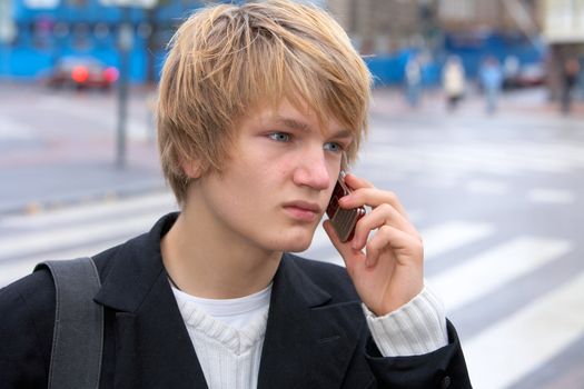 Teenage boy using mobile phone in street, looking away