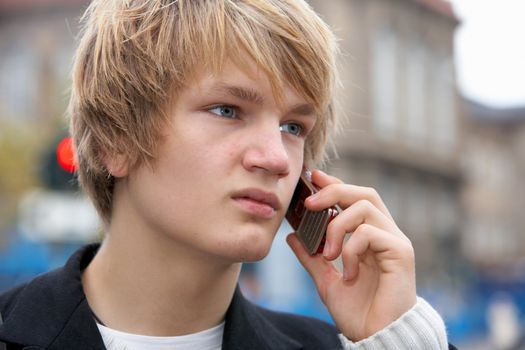 Teenage boy with mobile phone in street, looking away