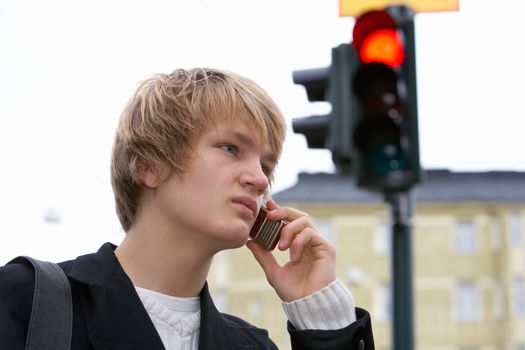 Teenage boy in street, using mobile phone, red light in background