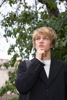 Teenage boy contemplating in city park, tree in background