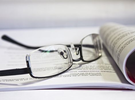 A pair of eye-glasses placed on book after hard reading.