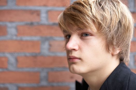 Thoughtful teenage boy by brick wall, close-up