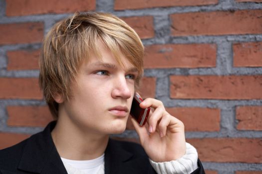 Teenage boy using mobile phone by brick wall, close-up