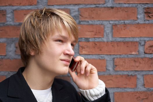 Teenage boy with mobile phone by brick wall