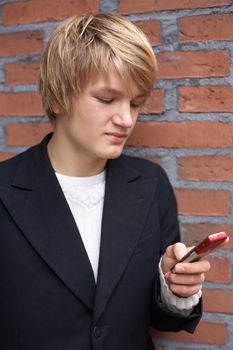 Teenage boy using mobile phone by red brick wall