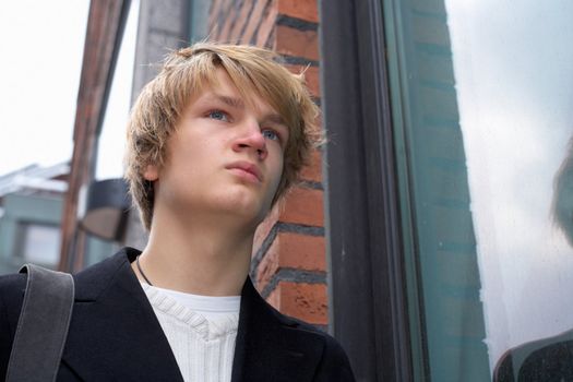 Teenage boy standing by window in street, low angle
