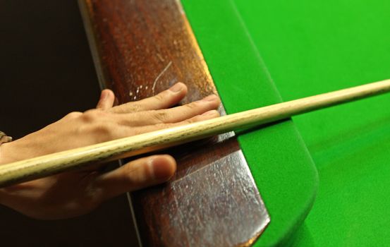 Young man concentrating while aiming at pool ball while playing billiards. 