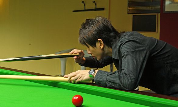 Young man concentrating while aiming at pool ball while playing billiards. 