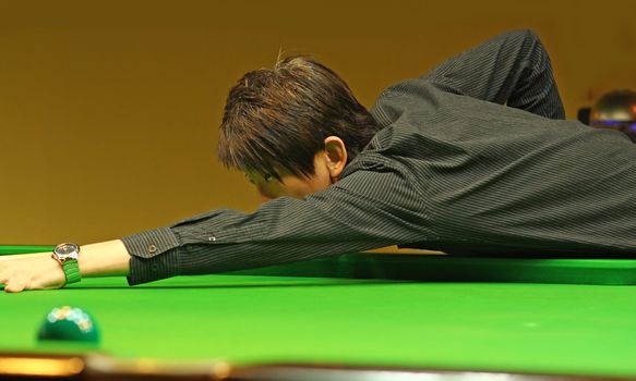 Young man concentrating while aiming at pool ball while playing billiards. 