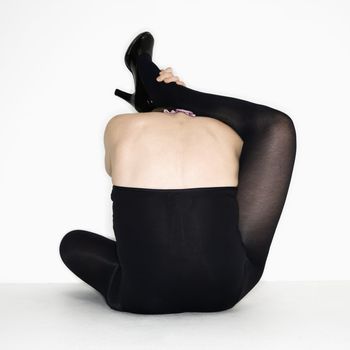 Portrait of young caucasian woman attempting to place her leg over her shoulders in a stretch.