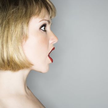 Profile portrait of young blonde caucasian woman who's mouth is open in shock.