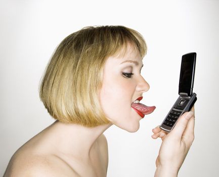 Side view of young blonde caucasian woman who is about to lick her cell phone.