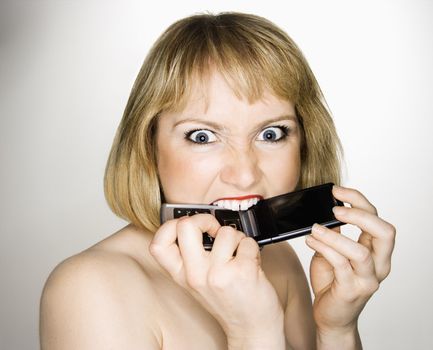 Portrait of young blonde caucasian woman who is biting her cellphone angrily.