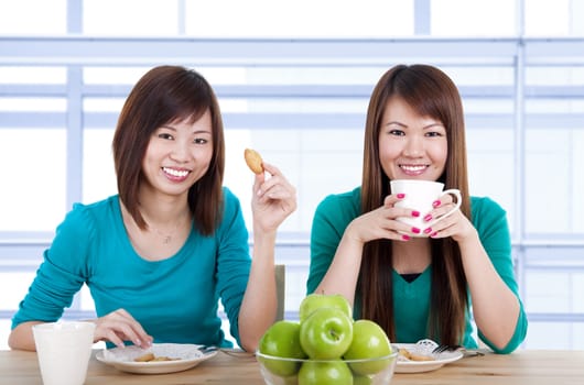 Two Asian women having tea break in home.