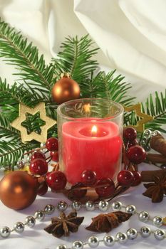 red candle with Christmas ball, stars and pine branches on a light fabric