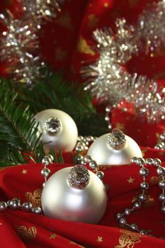 three silver Christmas balls and tinsel chain lie on red fabric